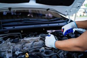 uma mecânico é trabalhando em uma carro motor, usando uma chave inglesa para afrouxar uma parafuso. conceito do foco e determinação Como a mecânico trabalho para consertar a carro foto