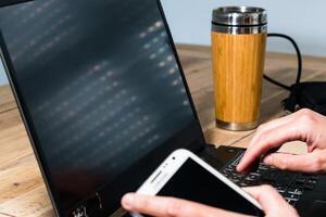 mulher usando Móvel telefone dentro a escritório com uma computador portátil e uma café foto