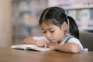 uma jovem menina é lendo uma livro às uma mesa foto