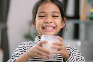 ásia pequeno fofa menina bebendo leite jovem pré escola criança menina ou filha permanece casa com uma sorridente face, sente feliz, e goza bebendo leite. foto