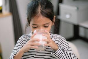 ásia fofa pequeno menina bebendo leite às a mesa às lar. goza bebendo leite. foto