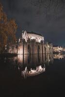 noite retrato do a medieval túmulo castelo dentro a Centro do Gante, Bélgica. a reflexão do a paredes é dentro a água canal foto