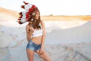 uma lindo jovem caucasiano menina dentro uma branco topo e jeans shorts. em dela cabeça vestindo a indiano chapéu barata. em pé dentro a deserto. foto