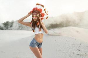 uma lindo jovem caucasiano menina dentro uma branco topo e jeans shorts. em dela cabeça vestindo a indiano chapéu barata. em pé dentro a deserto. foto