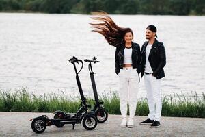 retrato do uma casal sentado perto elétrico patinetes, desfrutando Tempo dentro natureza junto, dois amantes em elétrico scooters.pessoas em patinetes foto