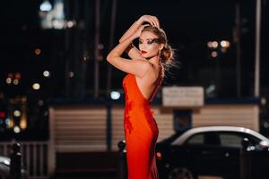 a elegante menina dentro uma vermelho tarde vestir em a ruas do a noite cidade do marselha.a mulher dentro uma vermelho tarde vestir dentro França foto