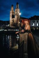 uma à moda noiva dentro uma Preto Casamento vestir e vermelho chapéu poses às noite dentro a velho cidade do zurique. retrato do uma modelo menina depois de pôr do sol.foto tiro dentro Suíça. foto