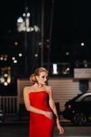 a elegante menina dentro uma vermelho tarde vestir em a ruas do a noite cidade do marselha.a mulher dentro uma vermelho tarde vestir dentro França foto