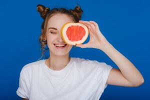 surpreso, a rindo menina detém a Toranja gostar ouvidos. vegano estilo de vida. sorridente mulher , comendo conceito.dieta orgânico , peso perda e saudável Comida. batidos e fresco suco. foto