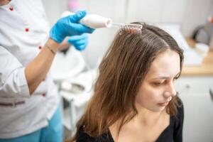 profissional esteticista fazendo darsonval cabelo tratamento procedimento para jovem mulher dentro beleza salão foto