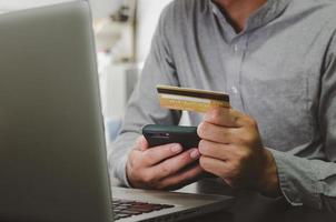 homem segurando a transação financeira do cartão de crédito ou compras online, usando o marketing online do computador. foto