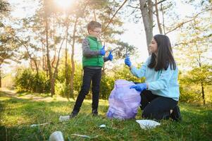 mulher voluntário e pequeno Garoto colheita acima a plástico lixo e colocando isto dentro biodegradável saco do lixo ao ar livre. ecologia, reciclando e proteção do natureza conceito. de Meio Ambiente proteção. foto