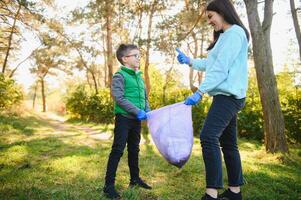 mulher voluntário e pequeno Garoto colheita acima a plástico lixo e colocando isto dentro biodegradável saco do lixo ao ar livre. ecologia, reciclando e proteção do natureza conceito. de Meio Ambiente proteção. foto