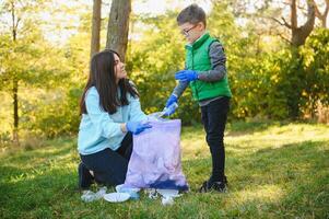 mulher voluntário e pequeno Garoto colheita acima a plástico lixo e colocando isto dentro biodegradável saco do lixo ao ar livre. ecologia, reciclando e proteção do natureza conceito. de Meio Ambiente proteção. foto