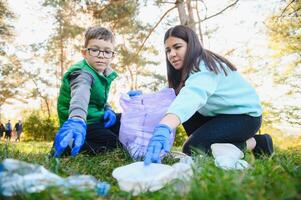 mulher voluntário e pequeno Garoto colheita acima a plástico lixo e colocando isto dentro biodegradável saco do lixo ao ar livre. ecologia, reciclando e proteção do natureza conceito. de Meio Ambiente proteção. foto