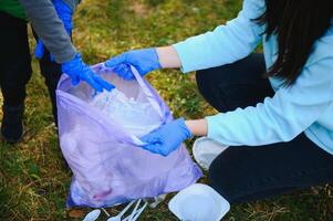 mulher voluntário e pequeno Garoto colheita acima a plástico lixo e colocando isto dentro biodegradável saco do lixo ao ar livre. ecologia, reciclando e proteção do natureza conceito. de Meio Ambiente proteção. foto