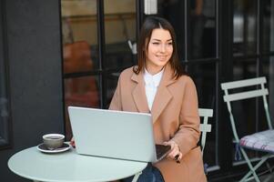 jovem bonita o negócio mulher trabalhando em computador portátil dentro rua cafeteria, digitando em teclado, inteligente senhora a sério olhando em tela.smartphone e óculos em mesa. vestindo à moda Rosa jaqueta, branco relógios. foto