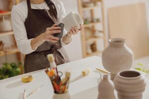 fechar acima do fêmea ceramista vestindo avental trabalhos com não disparado argila vaso dentro cerâmica estúdio foto