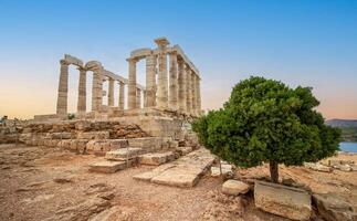 a famoso têmpora do Poseidon dentro Grécia com uma verde árvore às pôr do sol. dentro grego mitologia, a Deus do a mar. capa somião, ruínas do a antigo têmpora com azul céu foto