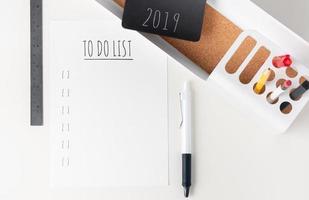 vista superior para fazer a lista de 2019 nota de papel em papelaria de escritório moderno em mesa branca. Lápis, bloco de notas, régua, caneta e caixa de lápis com plano foto