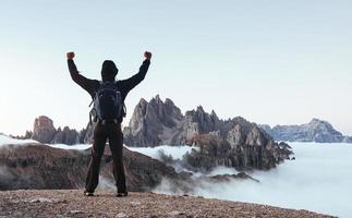 inspiração para o sucesso. homem turístico levantou as mãos sobre as belas montanhas cheias de nevoeiro à luz do dia foto