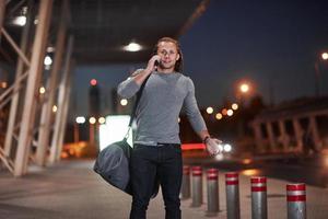 olhar satisfeito. homem com cabelo comprido e bagagem de viagem esperando o táxi buscá-lo