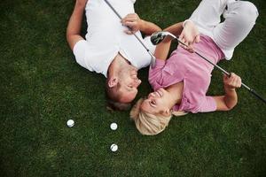 um casal, marido e mulher deitam no campo de golfe e relaxam após o jogo foto