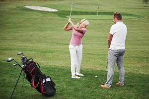 garota jogando golfe e rebatendo por taco no verde. sua professora ajuda a explorar a técnica e dar seus primeiros golpes foto