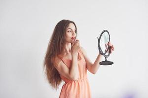 bela jovem segurando um espelho e fazendo maquiagem foto