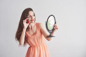 bela jovem segurando um espelho e olhando para a ferramenta de sobrancelhas