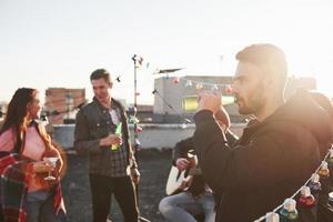 festa no telhado. amigos com álcool se divertindo. cara tocando violão foto