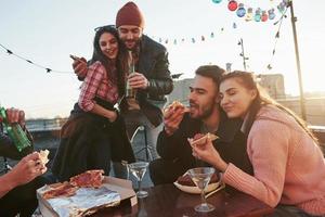 dois casais de pessoas adoráveis. comendo pizza na festa do telhado. bons amigos tenham fim de semana com comida deliciosa e álcool foto