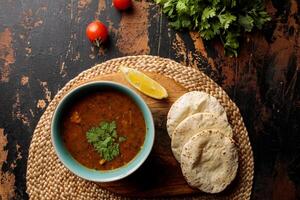 Harira sopa com pão, roti, Lima e tomate cereja servido dentro prato isolado em mesa topo Visão do árabe café da manhã foto