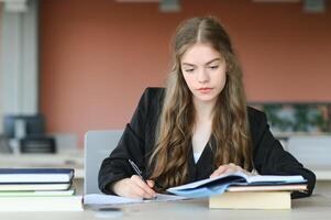 uma fofa 15 anos de idade estudante senta às uma escola escrivaninha com cadernos e livros e estudos foto