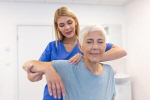 médico ou fisioterapeuta trabalhando examinando tratando ferido braço do Senior fêmea paciente, alongamento e exercício, fazendo a reabilitação terapia dor dentro clínica. foto