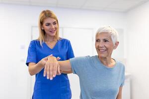 médico ou fisioterapeuta trabalhando examinando tratando ferido braço do Senior paciente, alongamento e exercício, fazendo a reabilitação terapia dor dentro clínica. foto