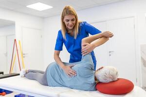 médico ou fisioterapeuta ajuda para curar uma Senior mulher voltar. e dar adendo dentro a reabilitação Centro. conceito do fisica reabilitação. foto