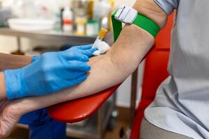 preparação para sangue teste com Senior mulher de fêmea médico médico uniforme em a mesa dentro branco brilhante sala. enfermeira pierces a pacientes braço veia com agulha em branco tubo. foto