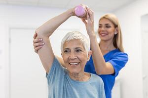 fisioterapeuta mulher dando exercício com haltere tratamento sobre braço e ombro do Senior fêmea paciente fisica terapia conceito foto