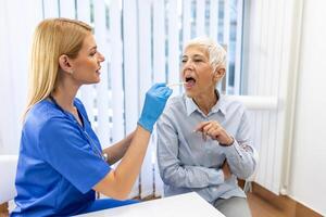 Senior paciente abertura dela boca para a médico para Veja dentro dela garganta. fêmea médico examinando dolorido garganta do paciente dentro clínica. otorrinolaringologista examina dolorido garganta do paciente. foto