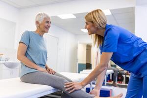 profissional ortopedista examinando Senior mulher pacientes perna dentro clínica. fisica terapeuta fazendo reabilitação procedimento para Senior mulher em massagem mesa. foto