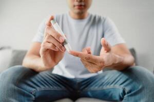 uma homem é sentado em uma sofá e segurando uma sangue açúcar teste dispositivo foto