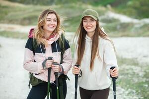 dois jovem mulheres amigos caminhantes com mochilas e caminhada postes em topo do uma montanha. viagem, viajante. foto