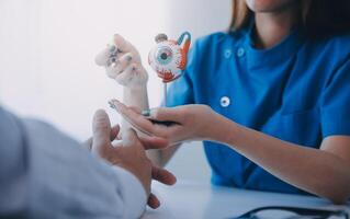 fechar-se do ásia fêmea médico falando com idosos paciente mostrando globo ocular modelo e explicando olho doença dentro hospital foto