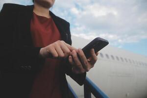 jovem ásia mulher dentro internacional aeroporto, usando Móvel Smartphone e verificação voar às a voar em formação borda foto