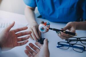 fechar-se do ásia fêmea médico falando com idosos paciente mostrando globo ocular modelo e explicando olho doença dentro hospital foto