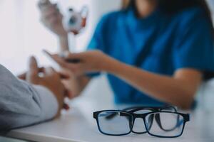 fechar-se do ásia fêmea médico falando com idosos paciente mostrando globo ocular modelo e explicando olho doença dentro hospital foto