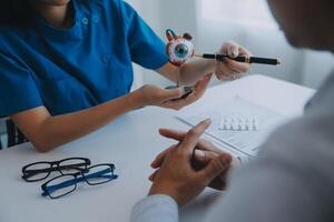 fechar-se do ásia fêmea médico falando com idosos paciente mostrando globo ocular modelo e explicando olho doença dentro hospital foto