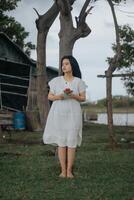 retrato do uma bonita jovem mulher vestido dentro branco vestir segurando rosa flores foto