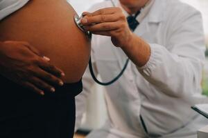 fêmea médico é verificação grávida mulher com estetoscópio. conceito carinhoso para grávida mulher foto